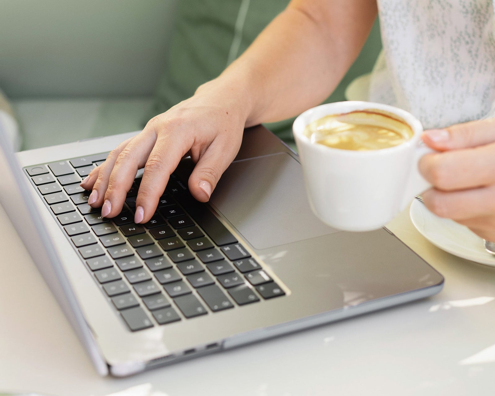 Web designer typing on computer, holding a cup of coffee